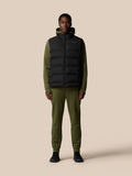 Full body shot of a model wearing a black heavyweight padded gilet over an olive green hoodie and joggers.