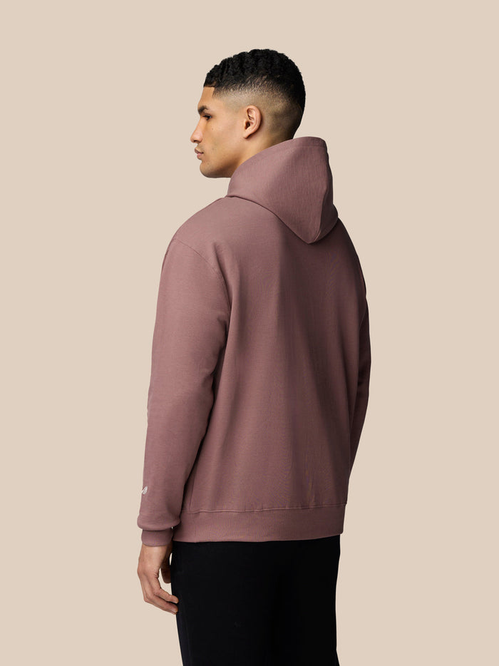 Back view of a model wearing mauve Adapt Lifestyle Hoodie with hood up and small logo on the sleeve.