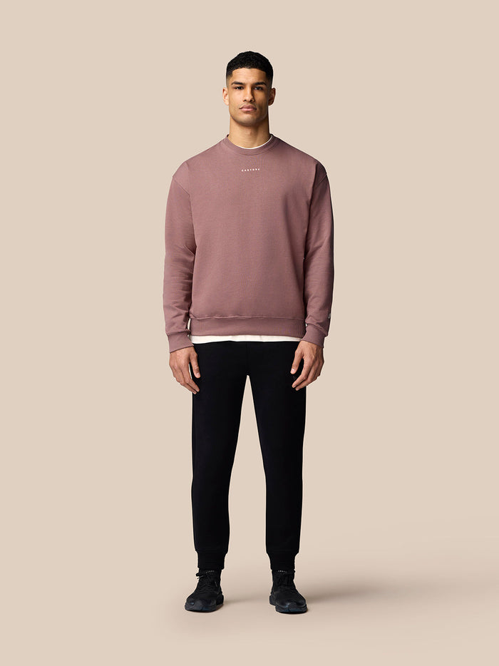 Male model in mauve oversized crew neck sweatshirt with black joggers and white sneakers
