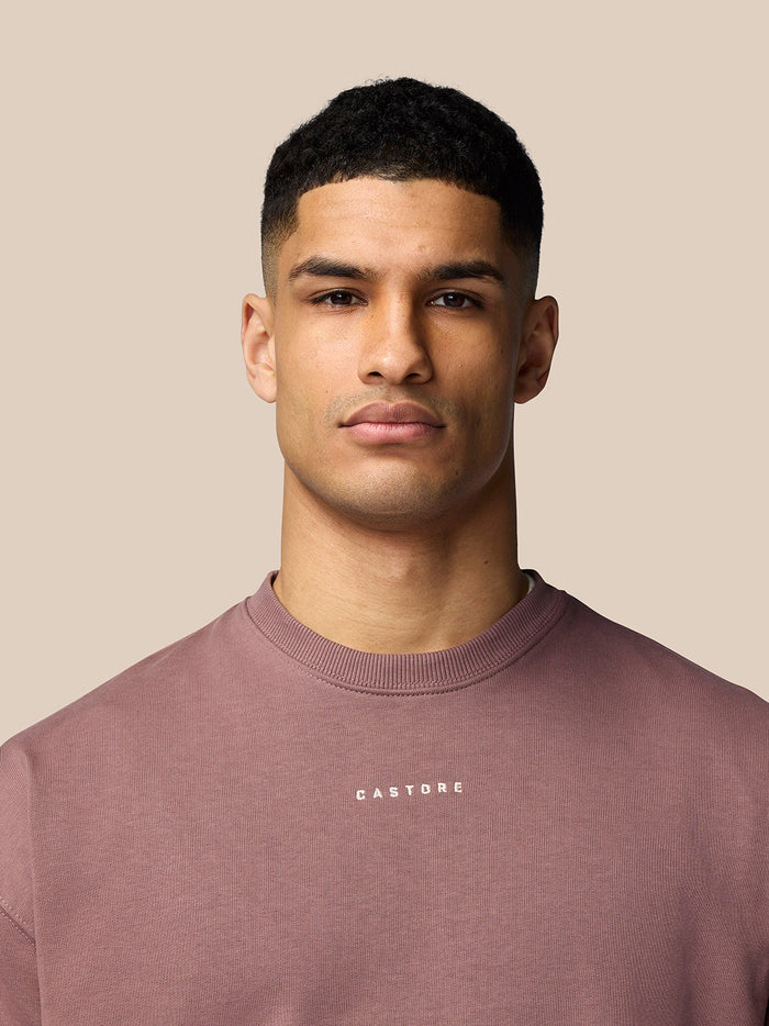 Male model wearing mauve Adapt Lifestyle Sweatshirt with crew neck and white Castore logo on the chest.