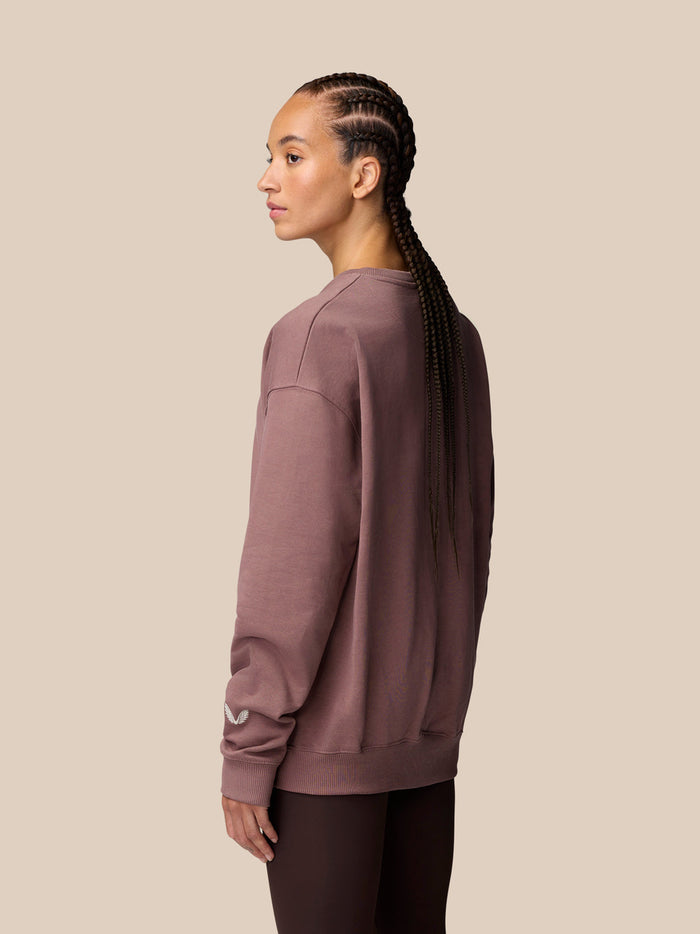 Profile view of model in mauve oversized sweatshirt showing left sleeve with Castore wings embroidery