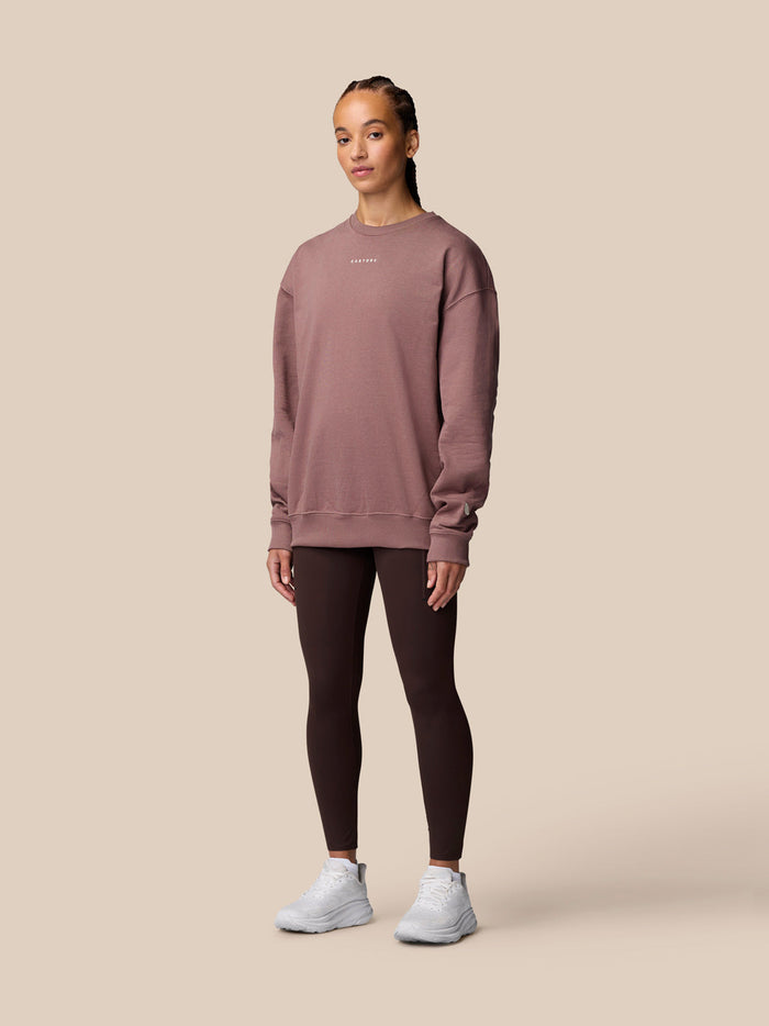 Full body shot of model in mauve oversized crew neck sweatshirt with dark leggings and white sneakers