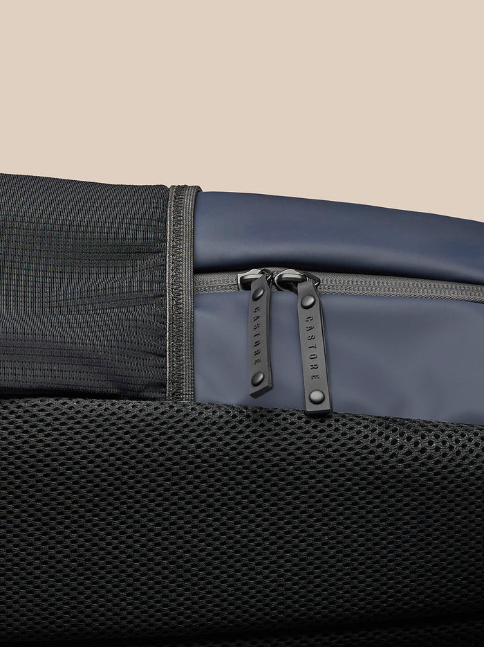 Close-up of navy Castore backpack showing twin zipper pulls and a black mesh pocket panel