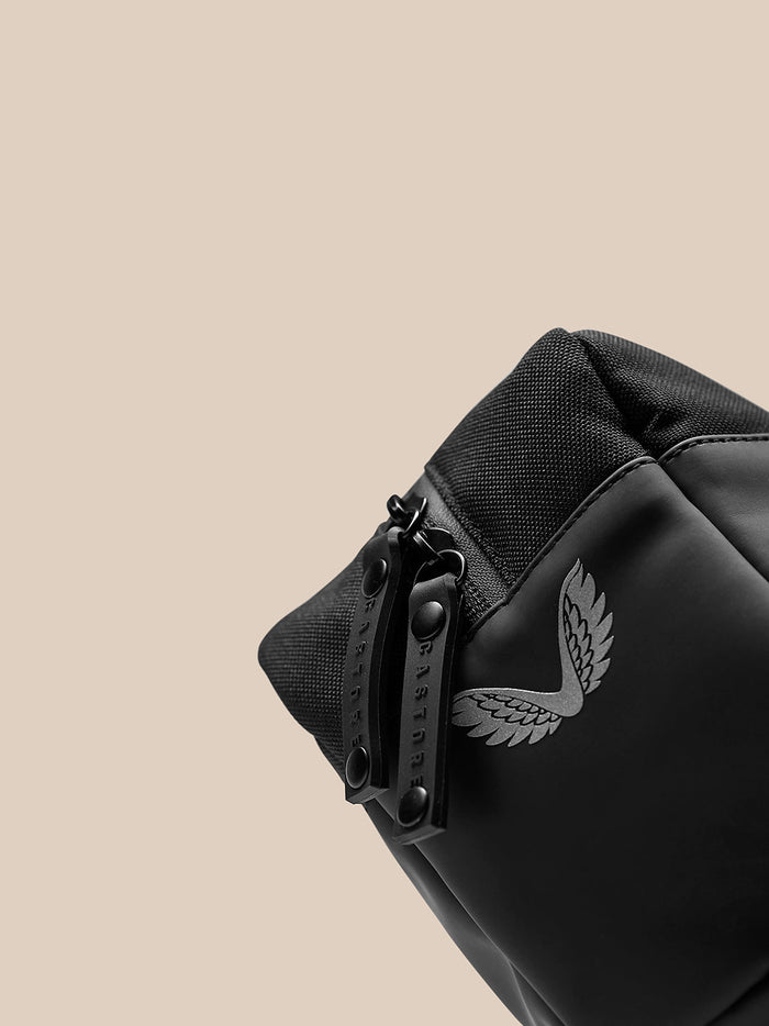 Detail view of zipper pull and wing emblem on the side of the black wash bag.