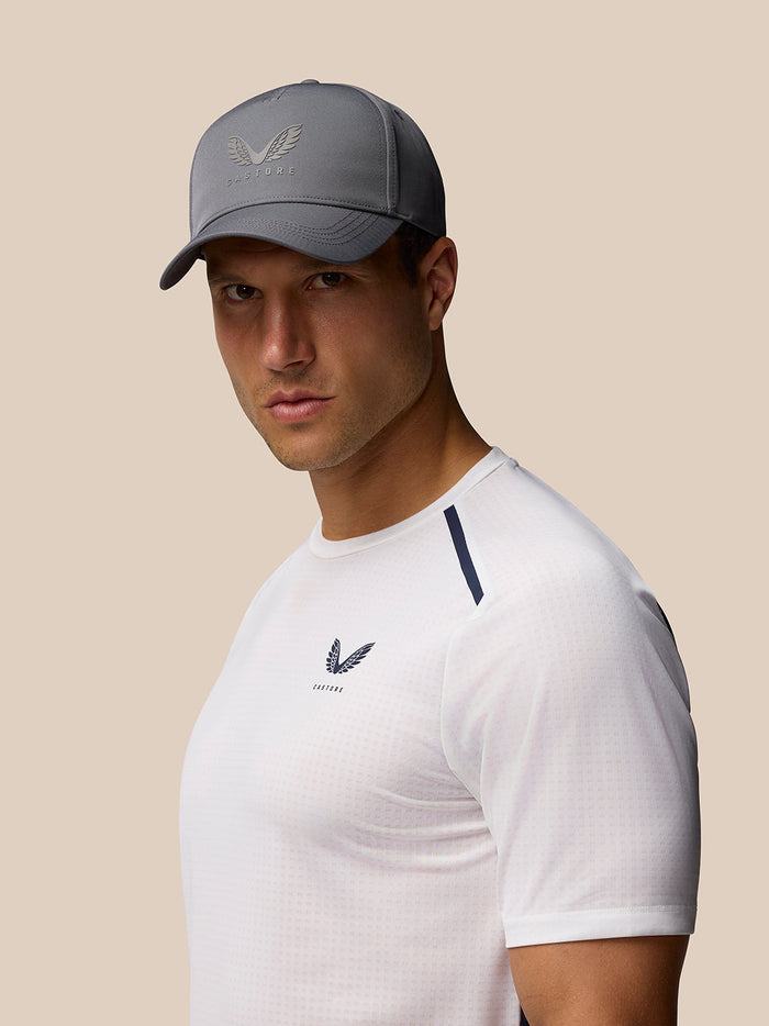 Man wearing a gray Castore logo cap with curved brim and front logo on a white shirt