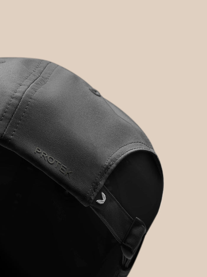 Close-up side view of gunmetal cap highlighting Protek branding and adjustable strap detail.