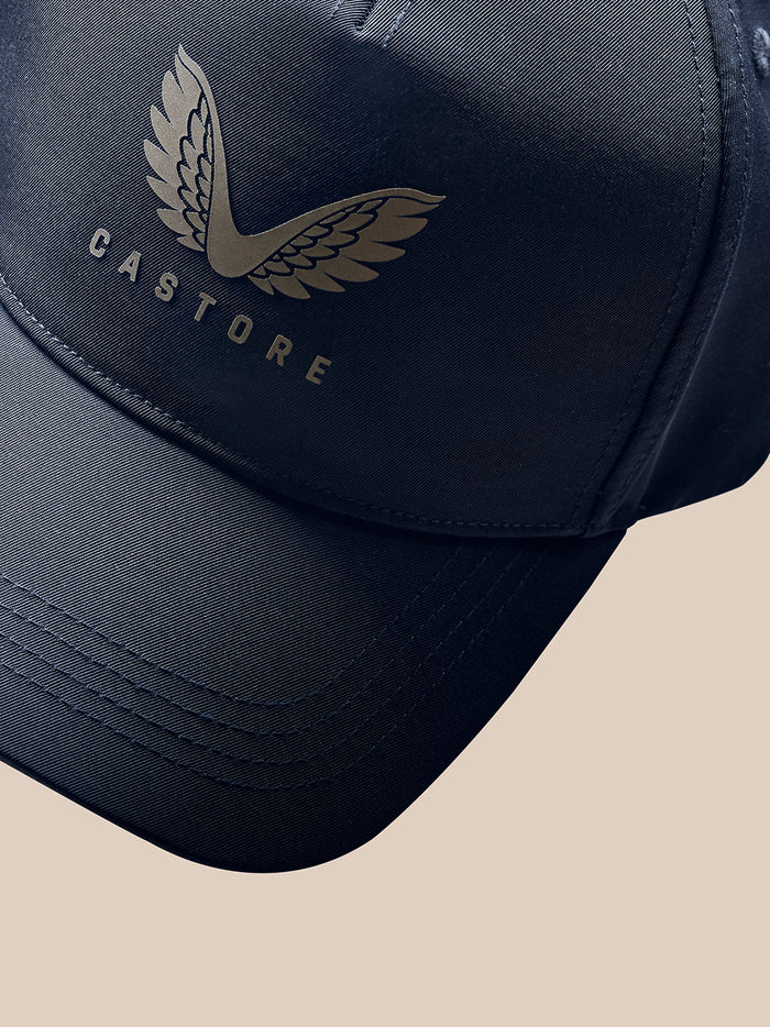 Profile view of a model wearing a navy Castore Core Cap with winged logo on the front and an adjustable back strap