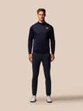 Full-body front view of a man in navy Castore golf outfit with a zip neck top and matching trousers