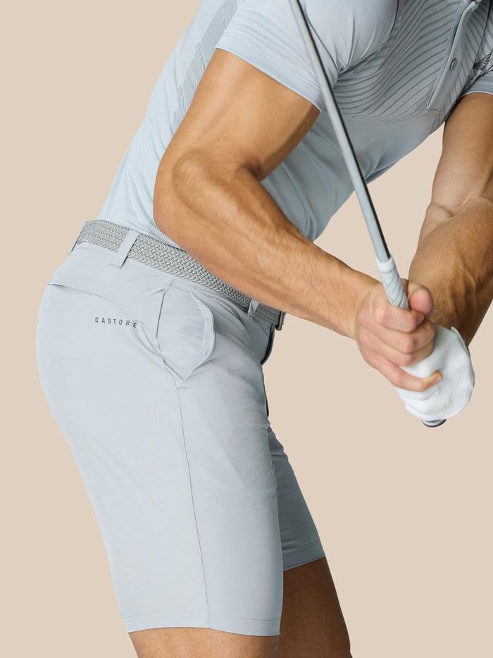 Side view of a male model wearing light grey golf shorts with a woven belt and Castore logo on the back right pocket