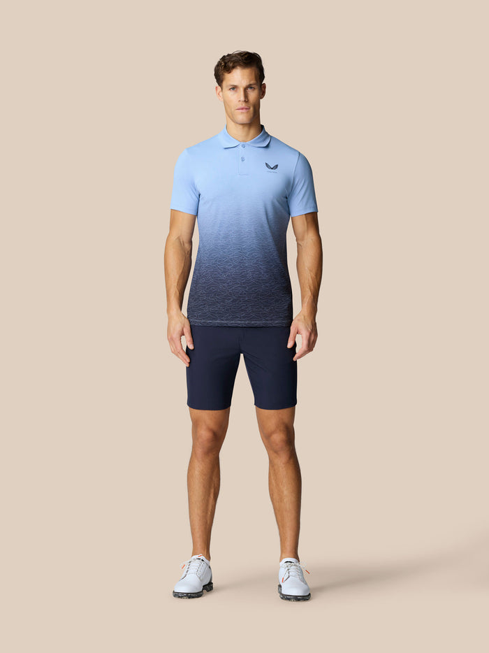 Male model wearing navy golf shorts with a light blue gradient polo against a beige background
