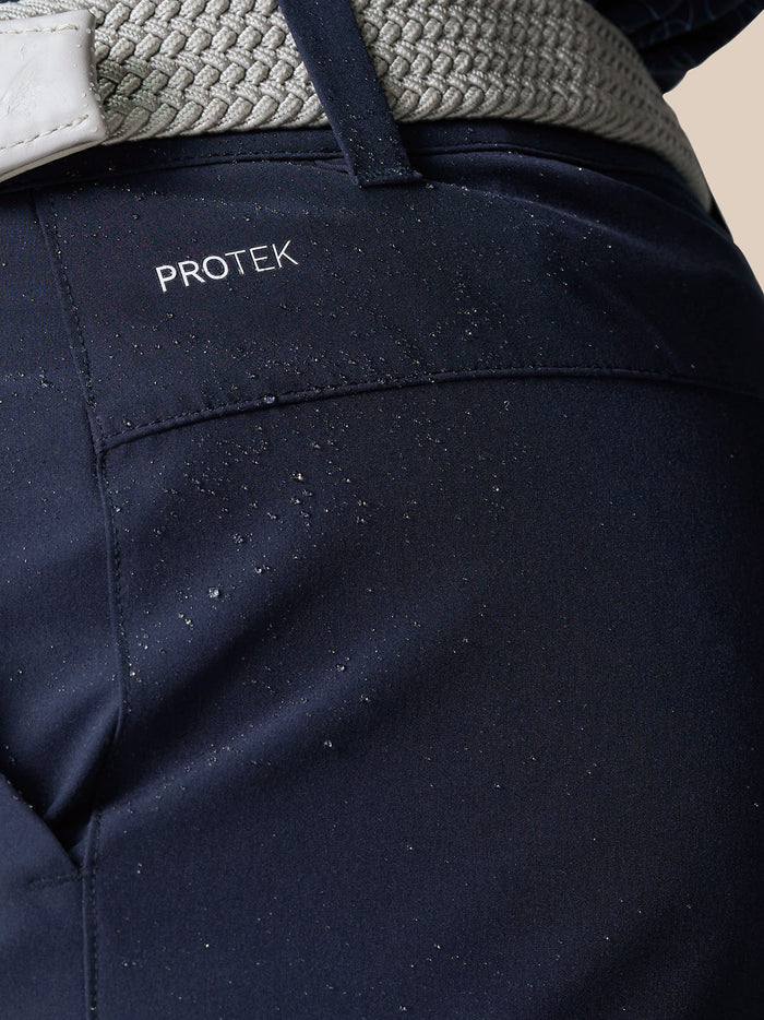 Rear waist close-up of navy Golf Club Shorts showing ProTek branding and the light gray belt.
