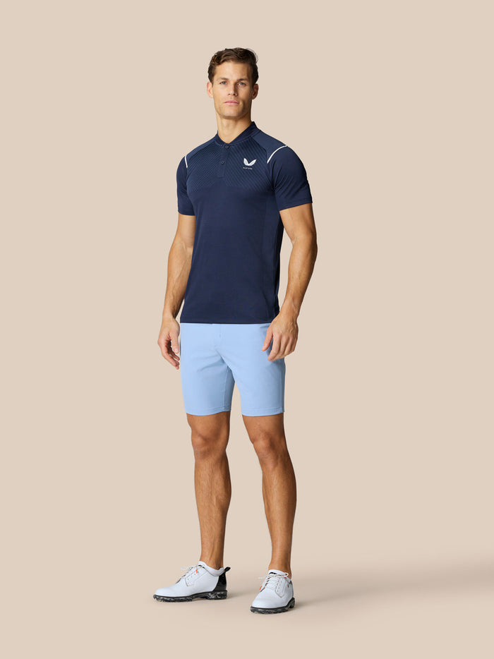 Male model wearing sky blue golf shorts paired with a navy polo on a beige background