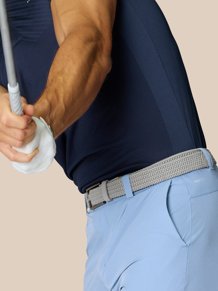 Back view of a golfer in sky blue shorts with a woven belt showing ProTek branding on the waistband.