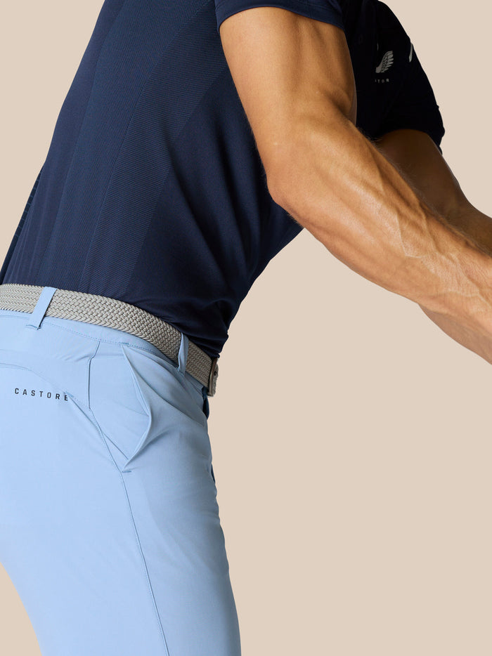 Side view of a golfer wearing a navy shirt and sky blue shorts with a woven belt and Castore branding on the thigh.