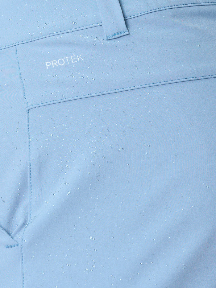Close-up of sky blue golf shorts fabric with ProTek branding and water droplets.