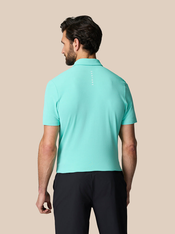 Back view of a man wearing a light aqua Golf Club Essential Polo with Castore branding down the spine.