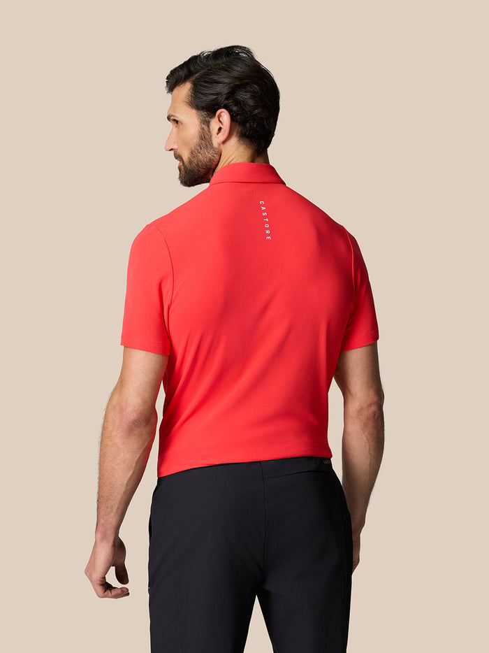 Back view of male model in Poppy red Golf Club Essential Polo with vertical Castore branding along the upper back.