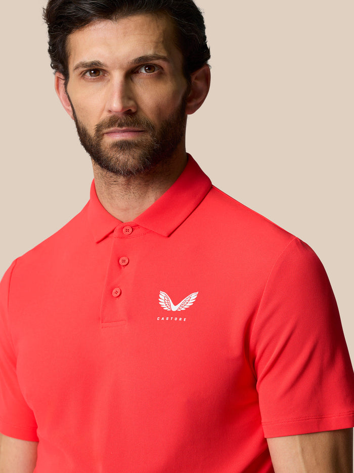 Close-up of male model wearing Poppy red Golf Club Essential Polo showing Castore logo on left chest.