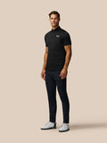 Full-length shot of a man in a black Pinnacle Pique Stripe Polo with dark trousers and white golf shoes
