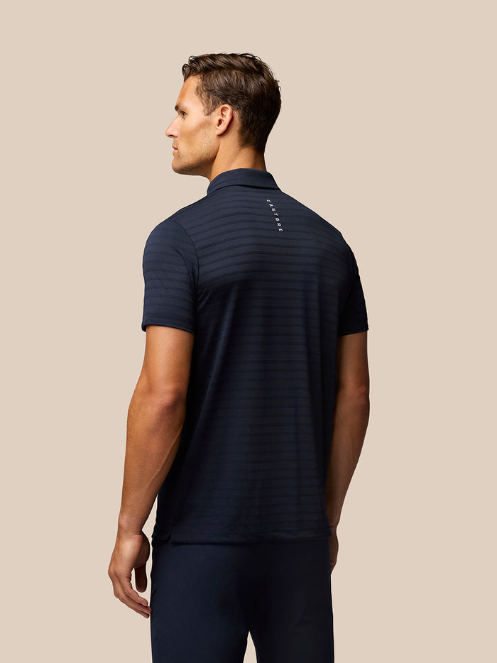 Back view of a man in a navy striped polo featuring vertical Castore branding along the upper back
