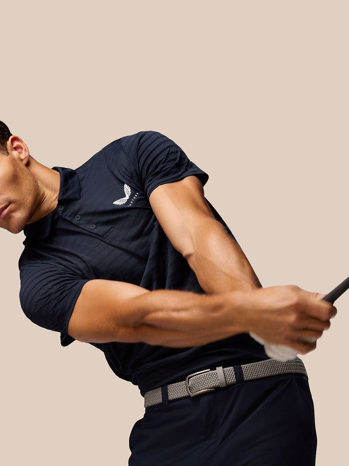 Three quarter view of male model in navy Pinnacle Pique Stripe Polo with stripe texture and Castore logo