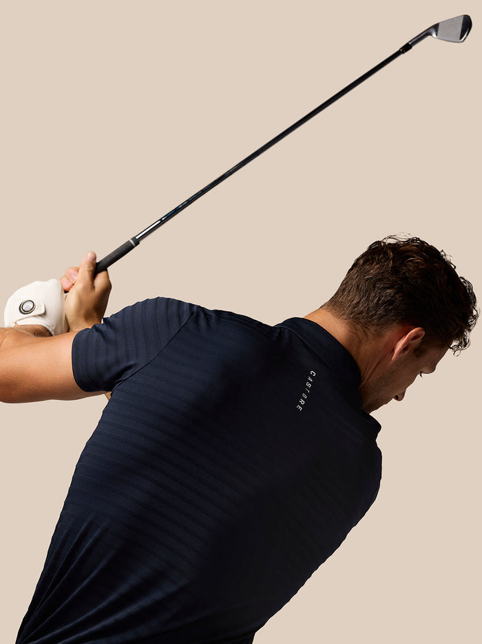 Golfer in navy Pinnacle Pique Stripe Polo mid swing with stripe pattern and Castore branding