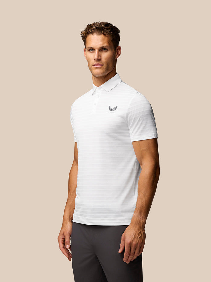 Male model wearing white Golf Pinnacle Pique Stripe Polo with subtle stripes and Castore logo on the chest against a beige background.