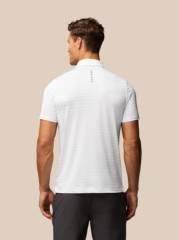 Back view of male model wearing white textured Pique Stripe Polo with Castore branding on the upper back.