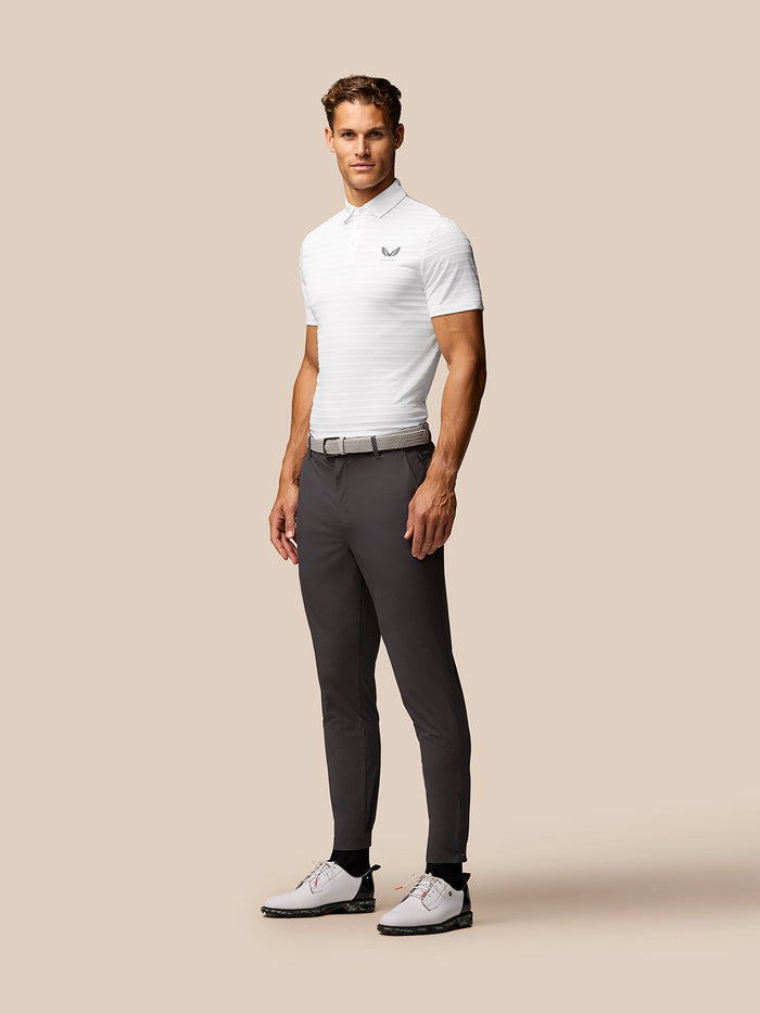 Rear view of male model in white textured polo with Castore branding on back, paired with gray trousers