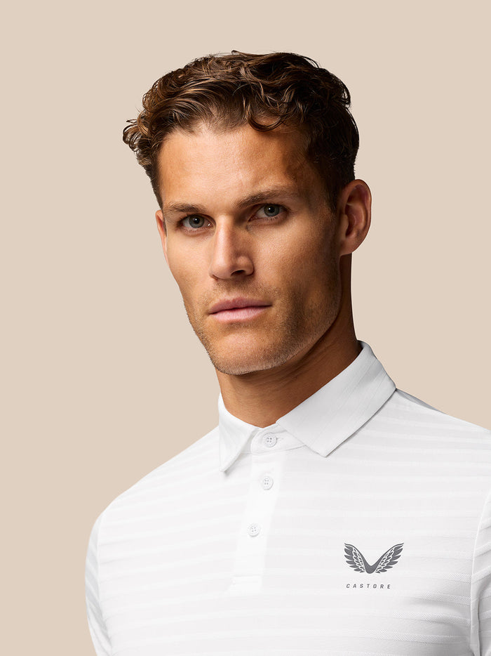 Close front view of male model in white textured stripe polo with Castore logo on the left chest.