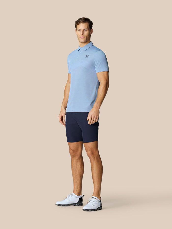 Male model wearing sky blue Golf Pinnacle Polo with navy shorts, showcasing breathable knit fabric.