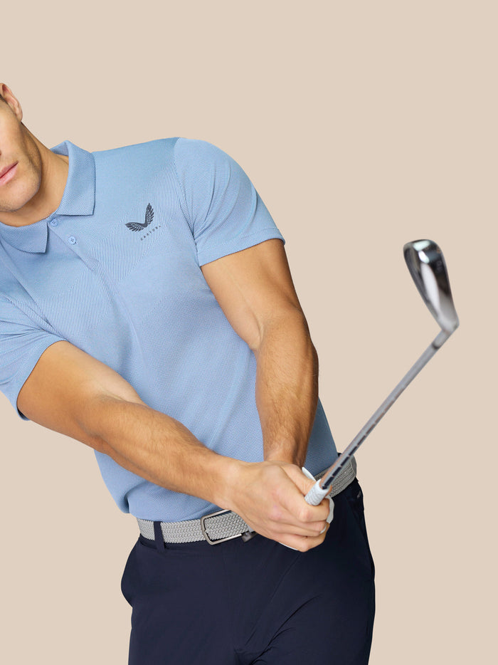Male model wearing sky blue Golf Pinnacle Polo during a golf swing highlighting breathable engineered knit fabric.
