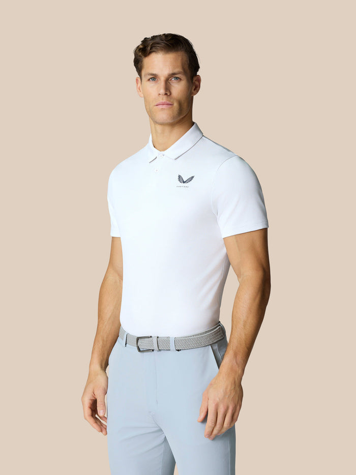 Male model wearing a white Golf Pinnacle Polo with short sleeves and light trousers.