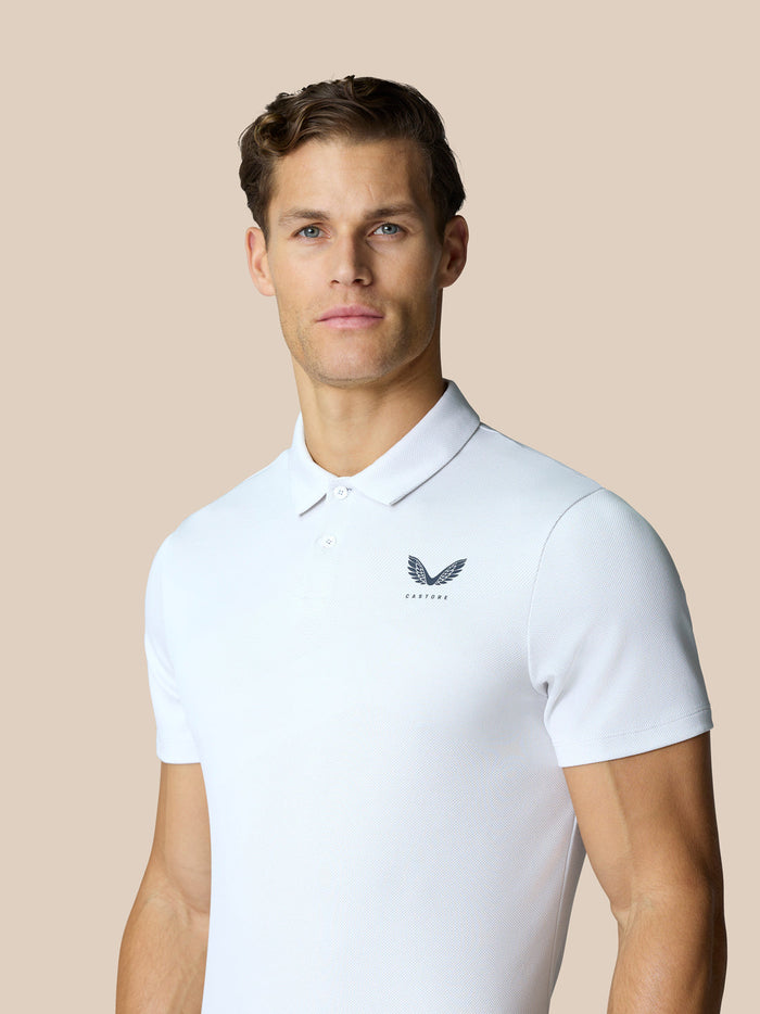 Male model wearing a white Castore Golf Pinnacle Polo with breathable knit fabric