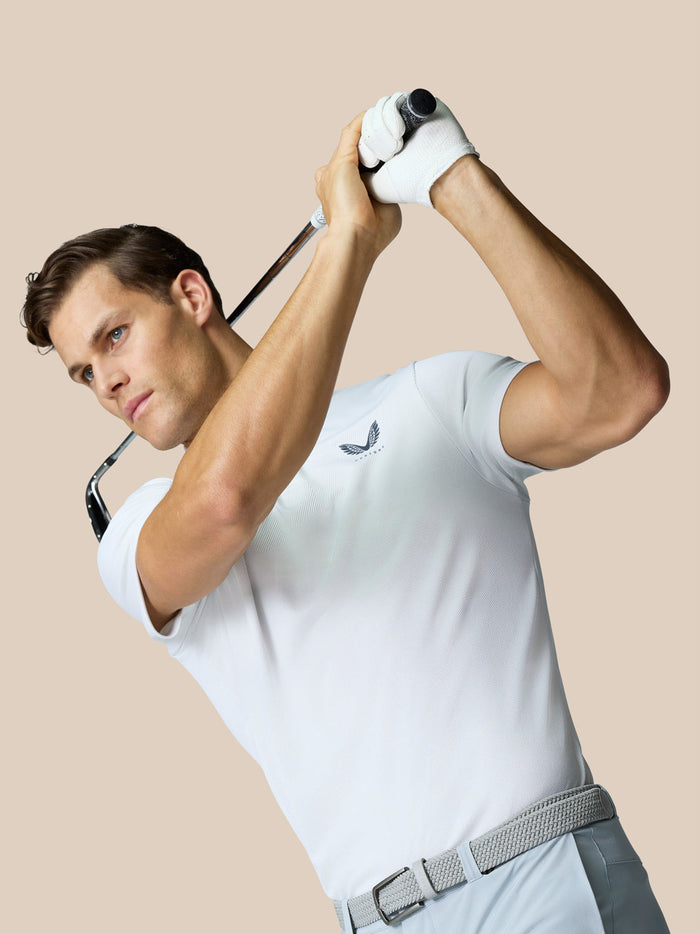 Golfer in a white polo mid swing holding a golf club with a small chest logo visible