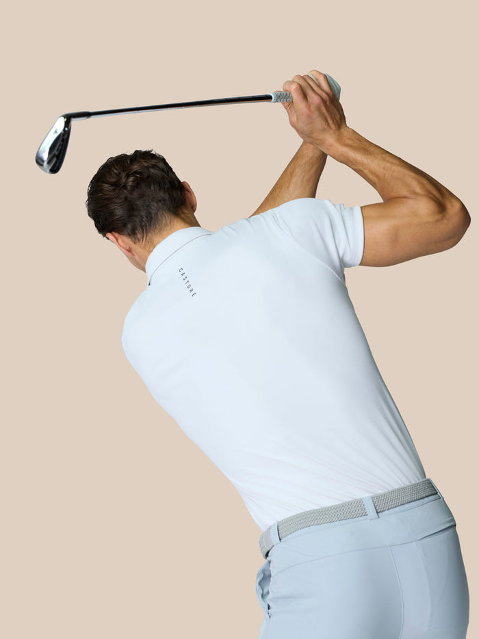 Back view of a male golfer in a white polo mid swing holding a golf club over his head