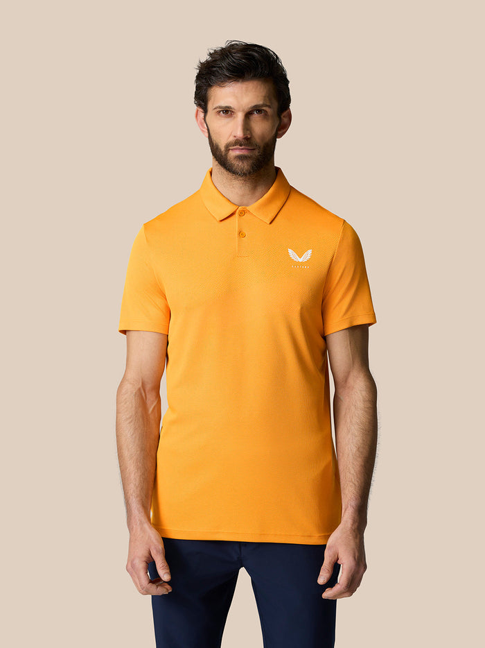 Male model wearing Mango Golf Pinnacle Polo in orange with a pointed collar and short sleeves.