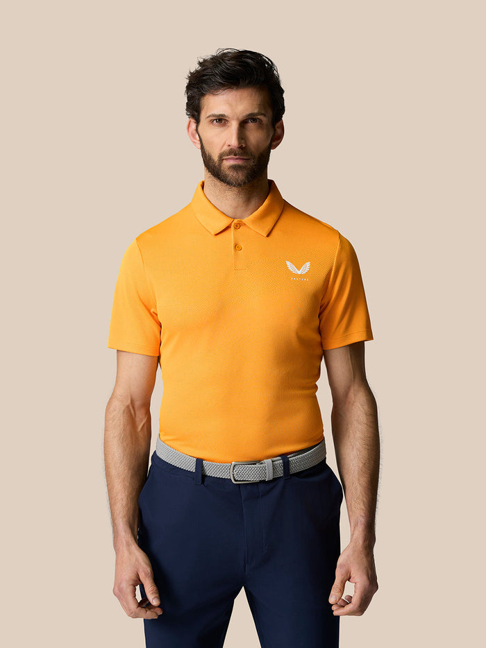 Front view of a male model wearing Mango Golf Pinnacle Polo in bright orange with a white Castore crest on the chest.