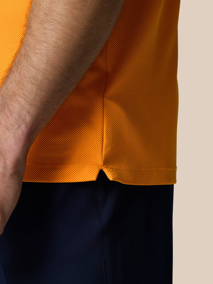 Close-up of mango orange polo knit showing textured fabric and side hem slit.