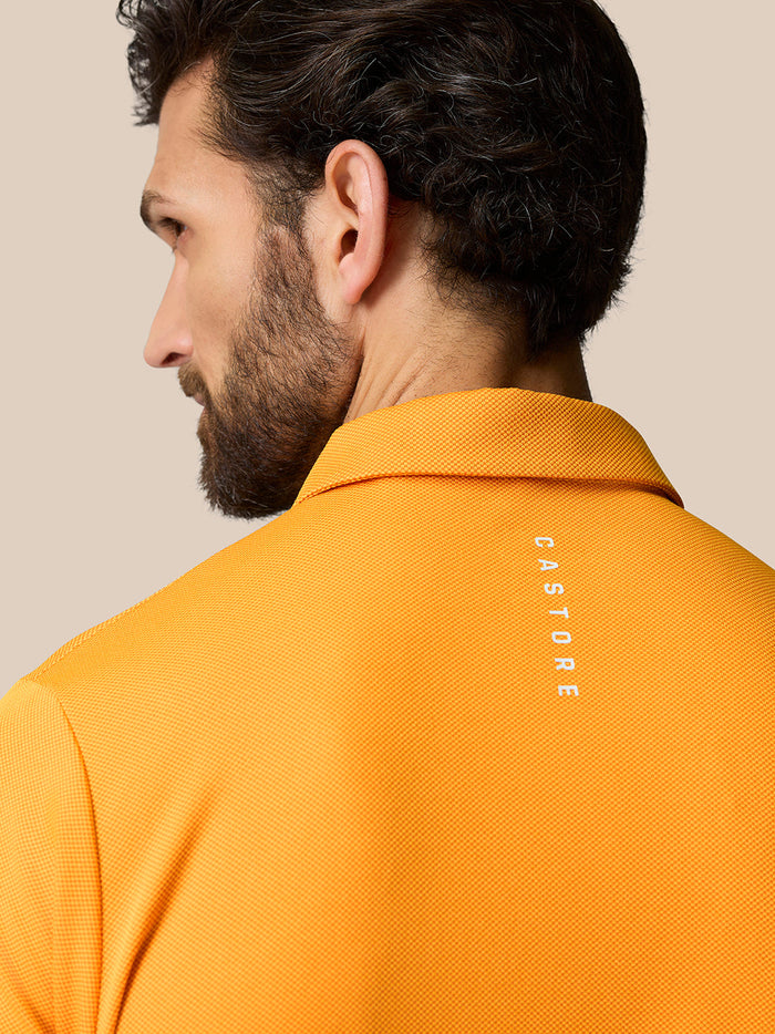 Back view of mango orange polo with Castore branding running down the upper back.