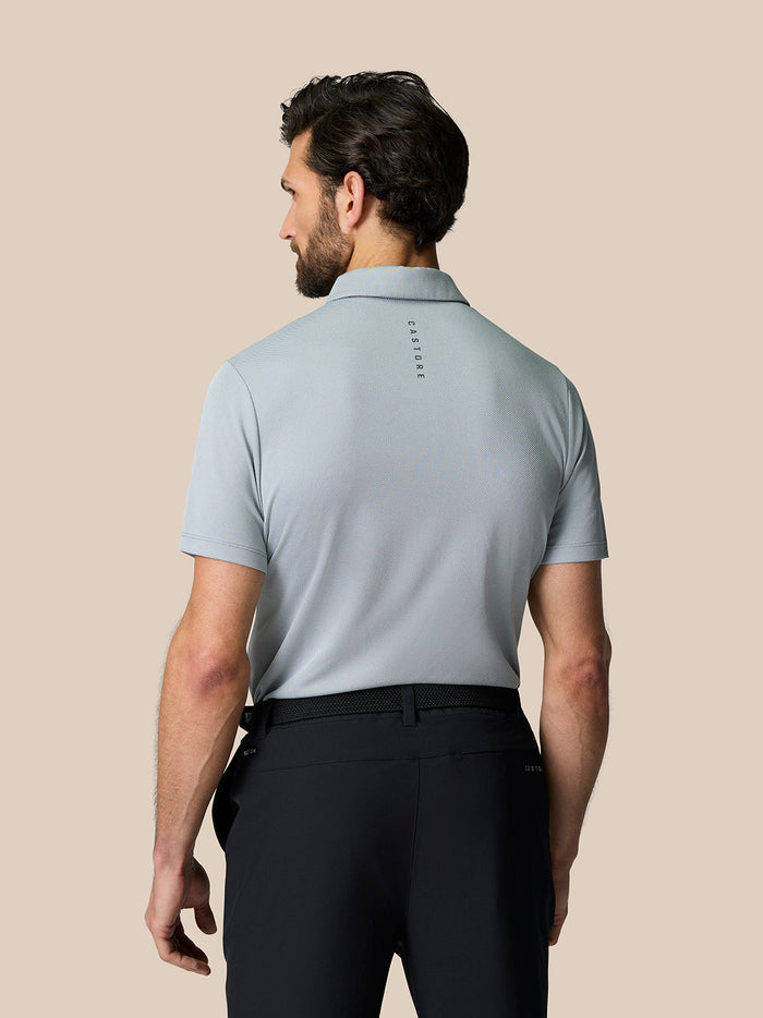 Back view of male model wearing light grey Engineered Knit Polo Top with branding along the upper back
