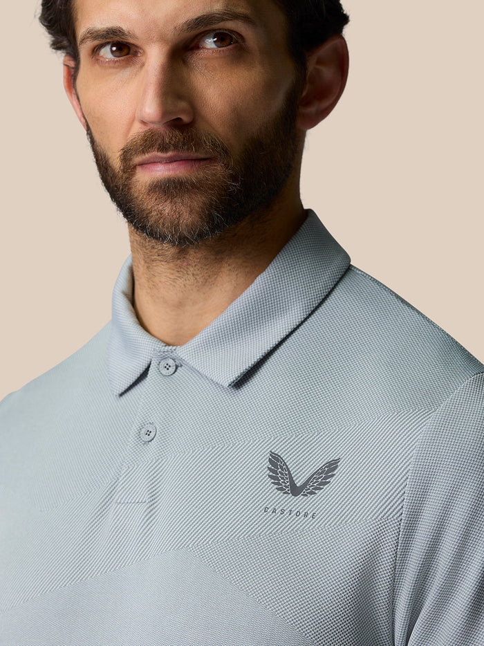Close-up of a man wearing a light grey textured polo with a pointed collar and Castore logo on the chest.