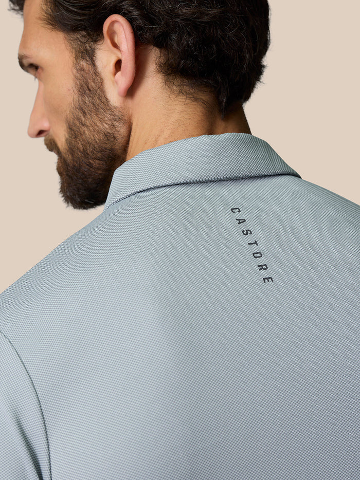 Back view of a man wearing a light blue textured polo with Castore branding on the upper back.