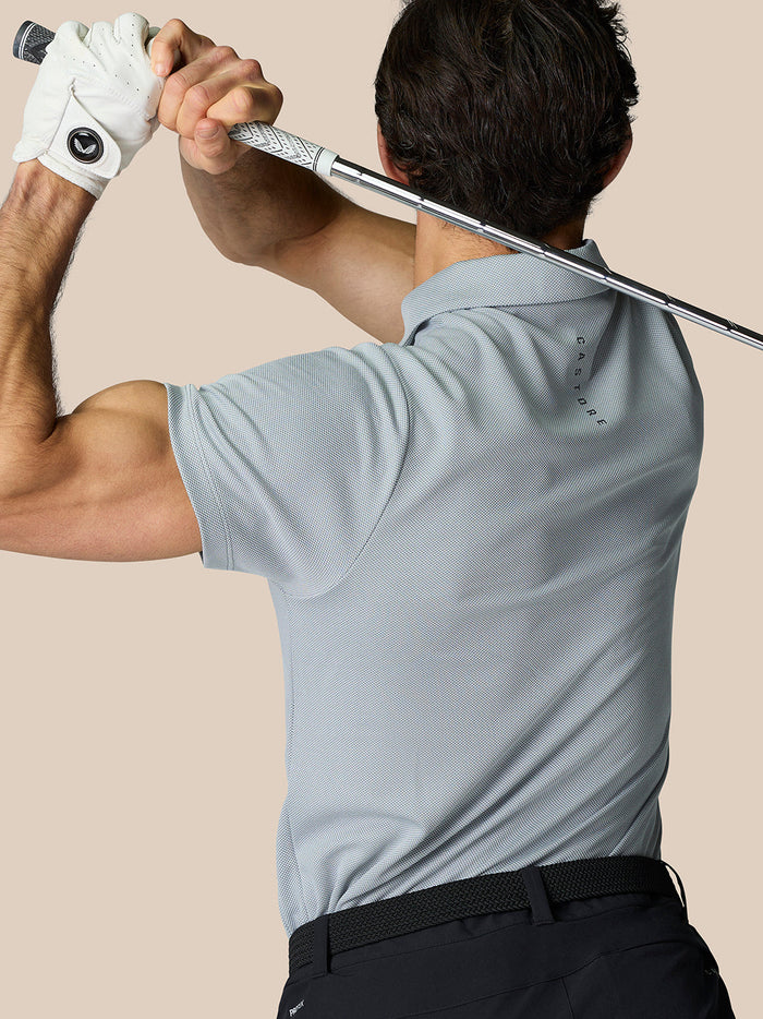 Back view of male golfer wearing light blue Castore polo while swinging a club