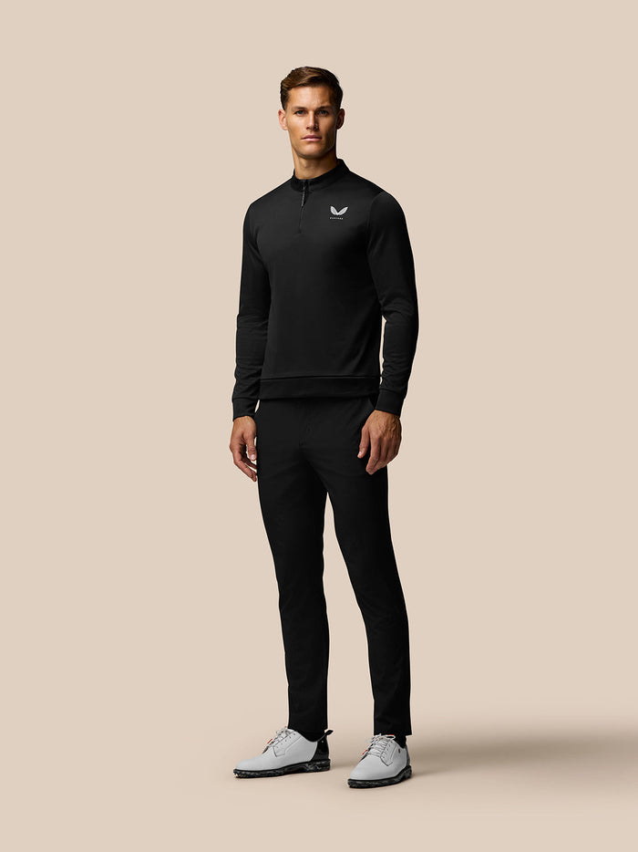 Full body shot of a man wearing a black Golf Club Classic 1/4 Zip Top with stand collar on a beige background
