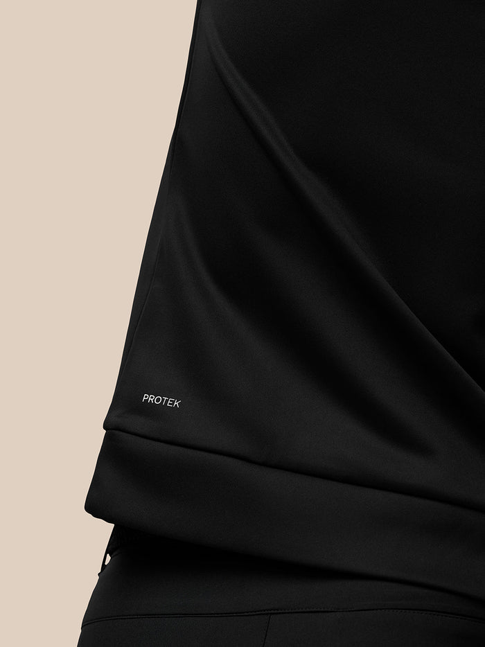 Close-up of the Protek branding on the lower left back hem of the black Golf Club Classic top