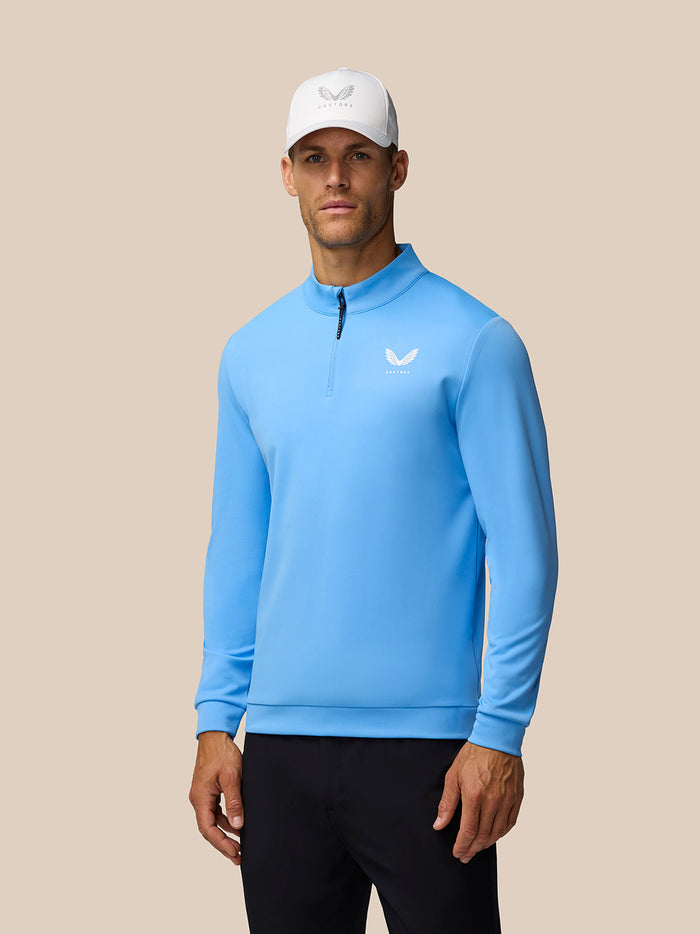 Male model wearing light blue Golf Club Classic 1/4 Zip Top with funnel collar and white cap