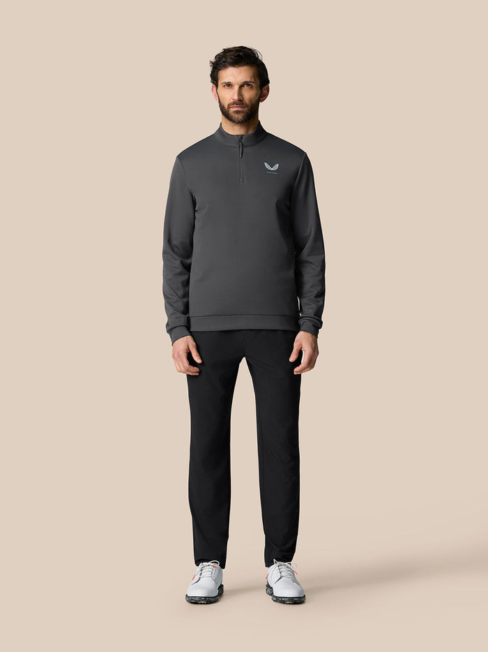 Full-body view of a man wearing the gunmetal Golf Club Classic Quarter Zip Top with wing logo on the chest, paired with black pants and white sneakers.