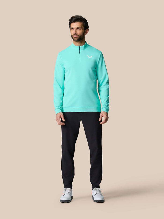 Full-length shot of a man wearing the light aqua Golf Club Classic Quarter Zip Top with stand collar and black trousers.