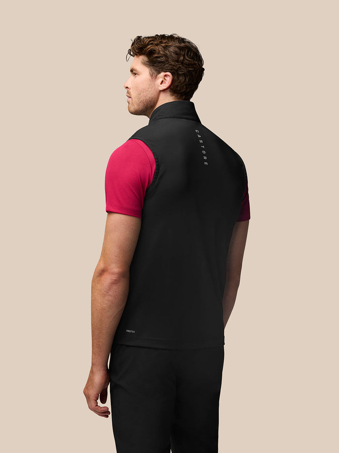 Back view of a man in a black Castore Golf Pinnacle Gilet over a pink polo, with vertical branding along the upper back
